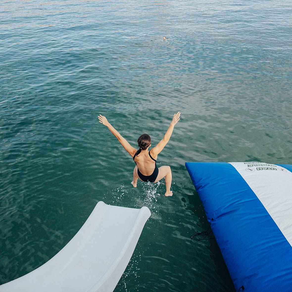 A woman jumps slides off a waterslide on the side of a houseboat.