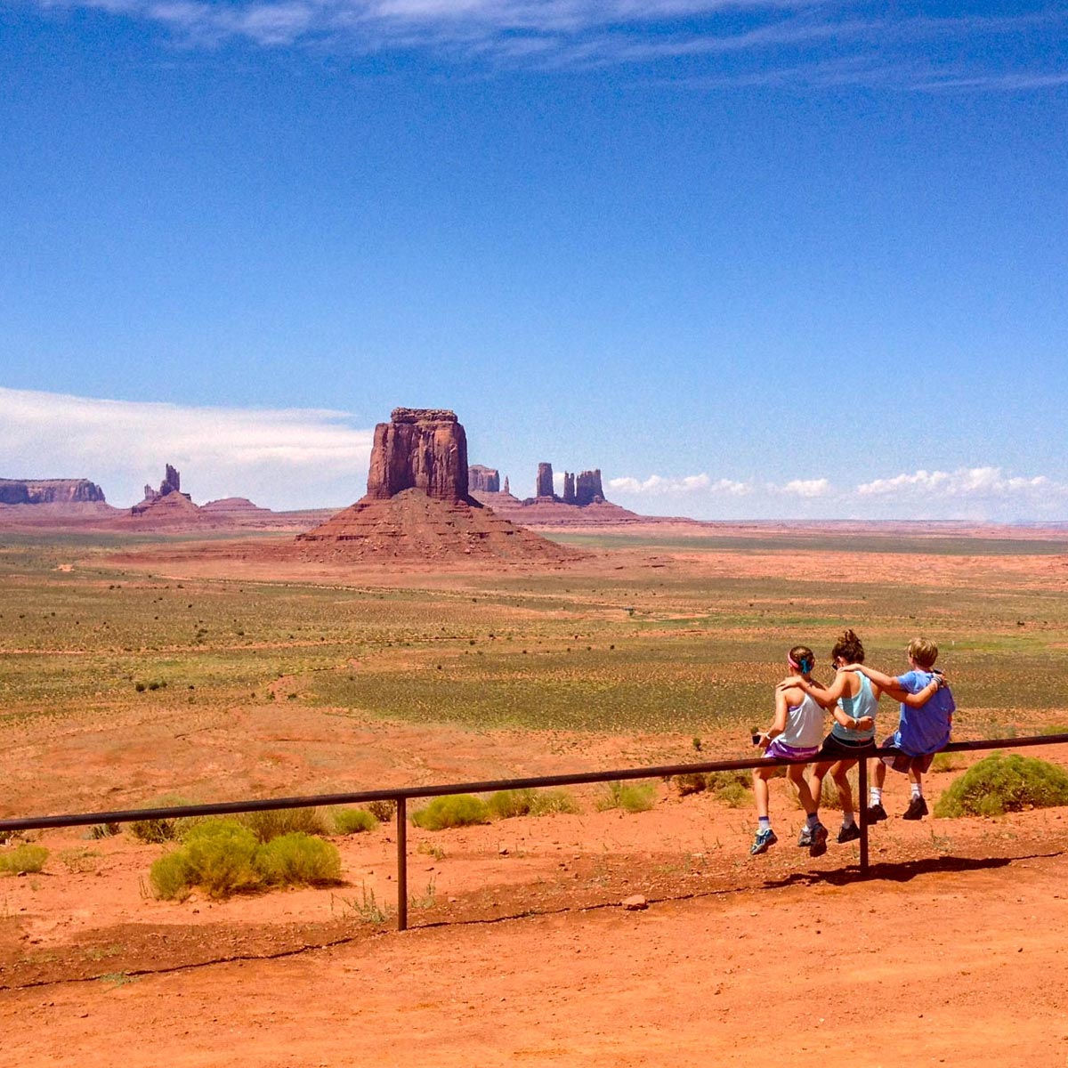 Three children sit on a railing looking at Monument Valley.