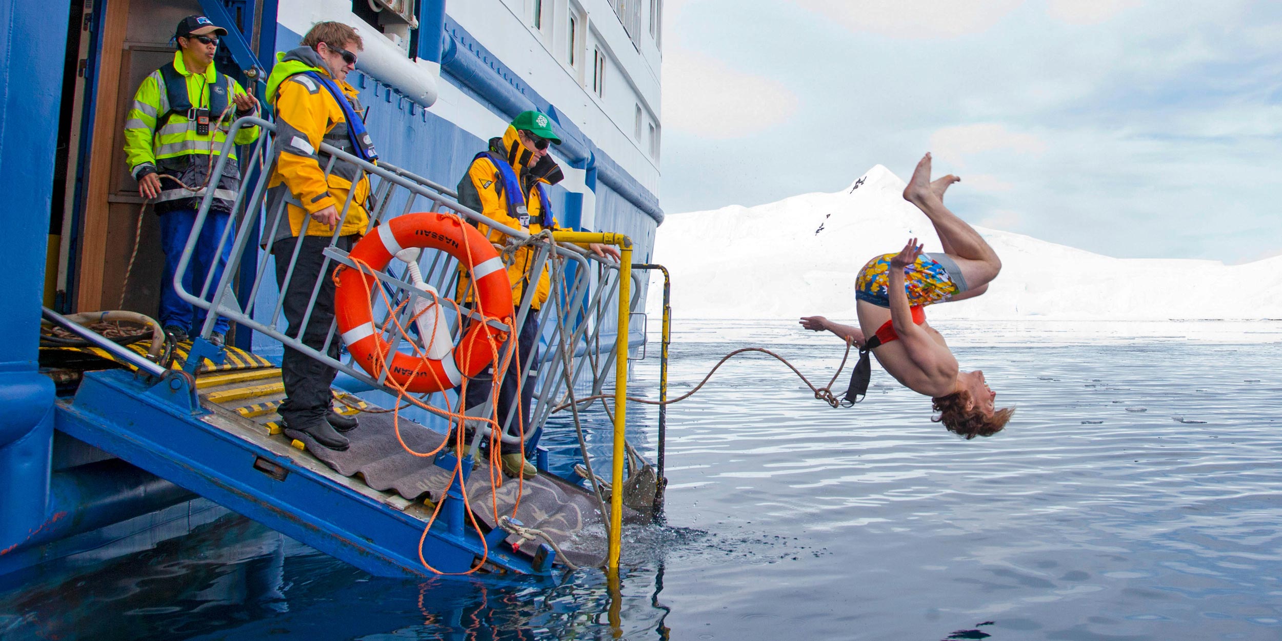 A person doing a flip into the icy Antarctic water for a polar plunge, watched by expedition staff.