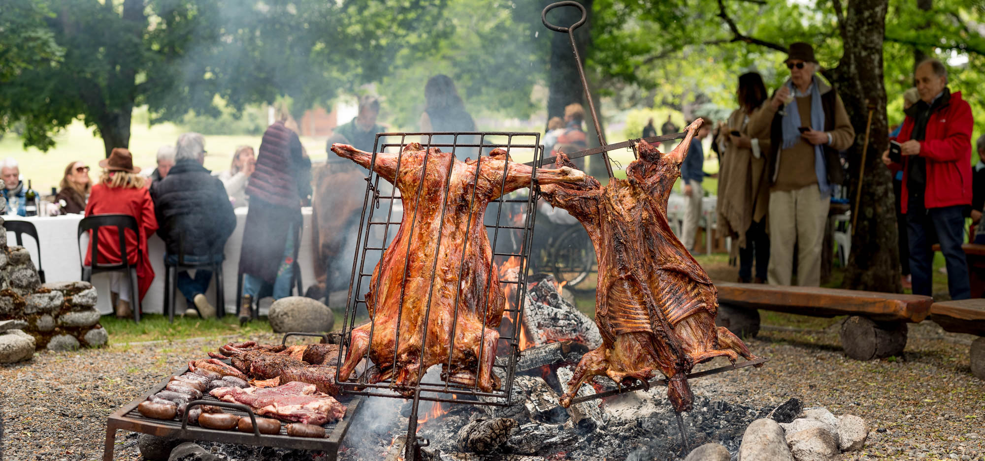 Two whole animals (likely lambs or goats) roasting vertically on a metal cross over an open fire (asado).