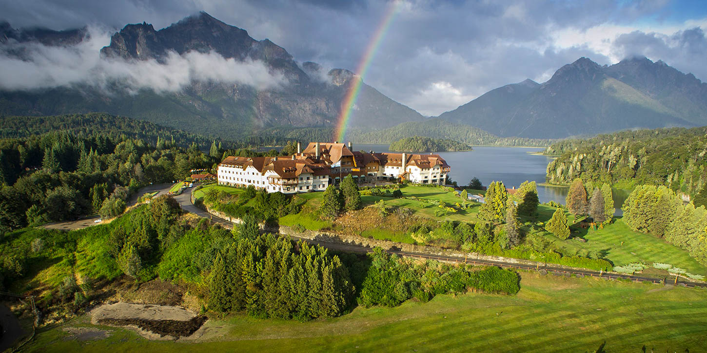 Panoramic view of Llao Llao Hotel in Bariloche, set on a peninsula with a lake, mountains, and a rainbow.