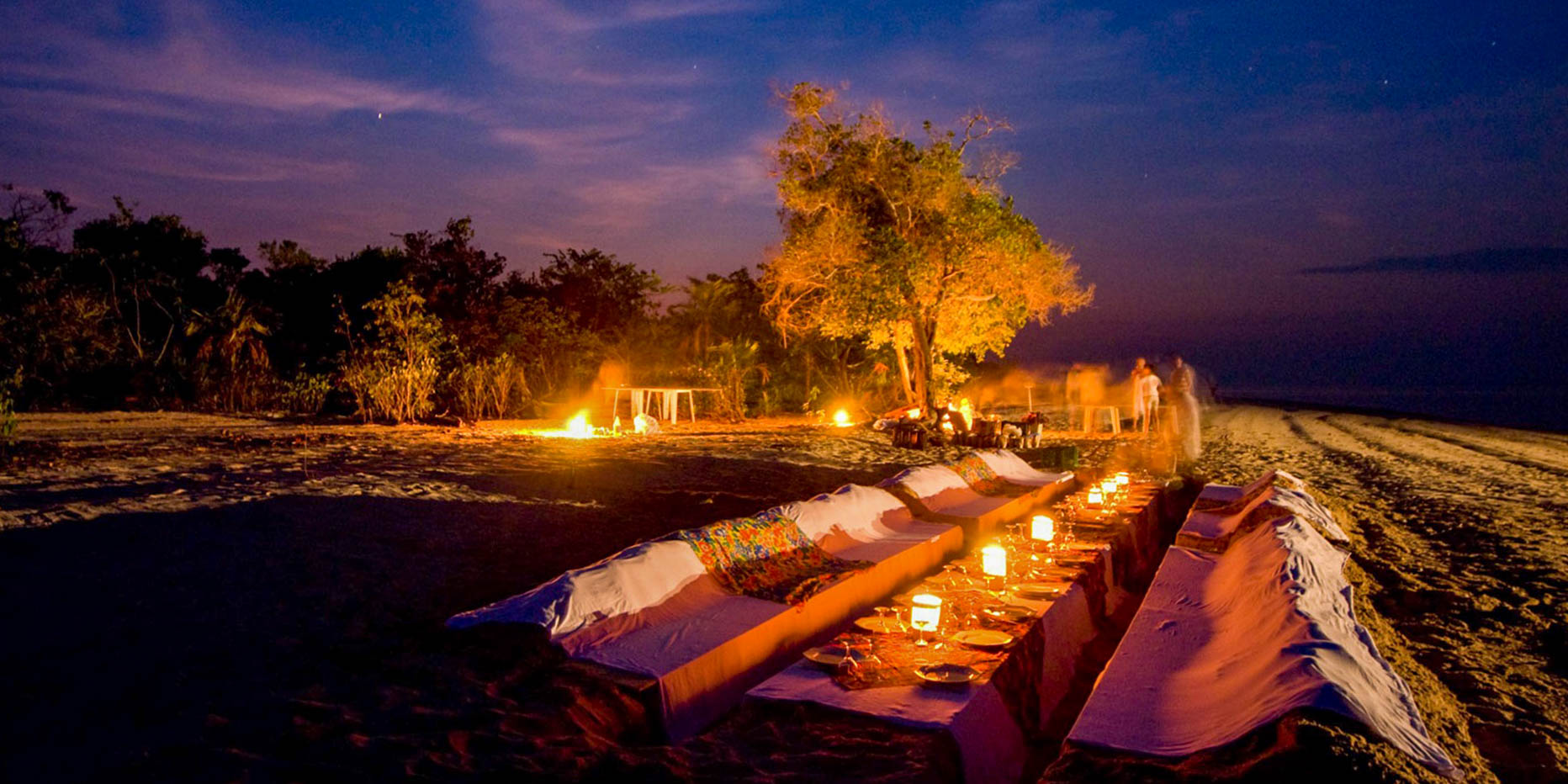Candlelit private dinner set up on a wide, dark beach next to the Rio Negro in the Brazilian Amazon.