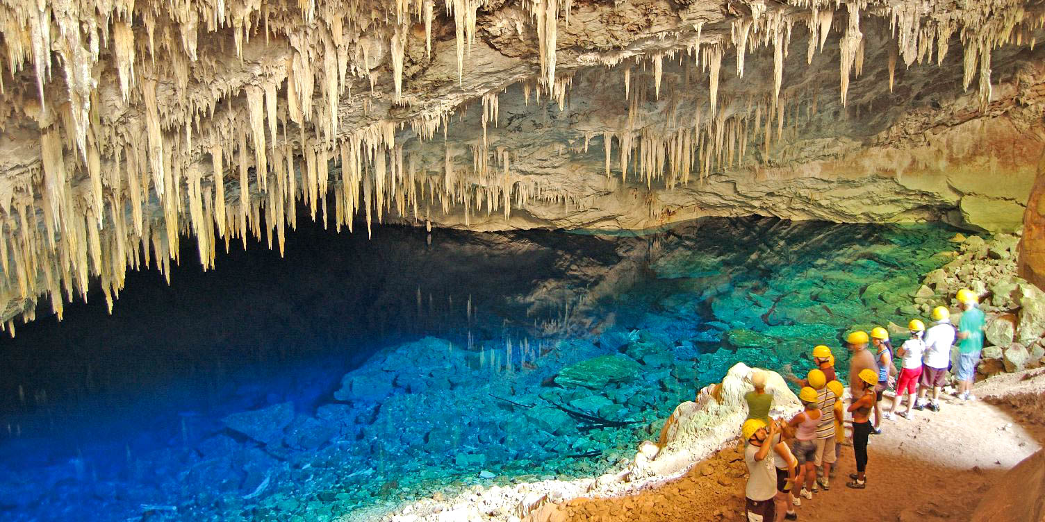 Visitors in hard hats viewing the vivid blue water inside the Gruta do Lago Azul cave in Bonito, Brazil.