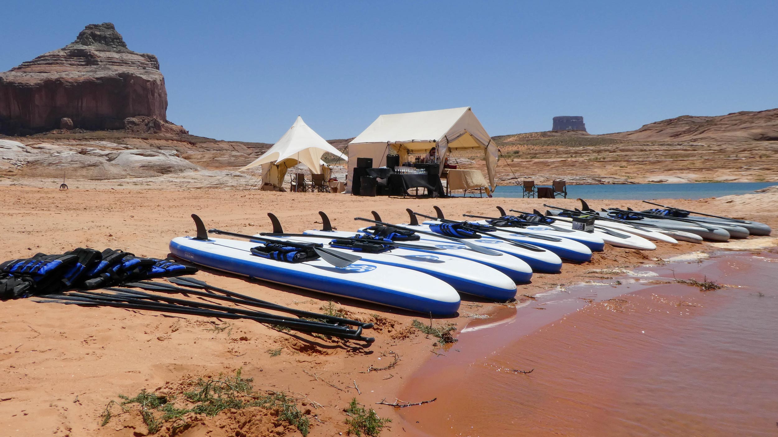 Paddle boards sit on the shore on Lake Powell with a private rest area nearby.