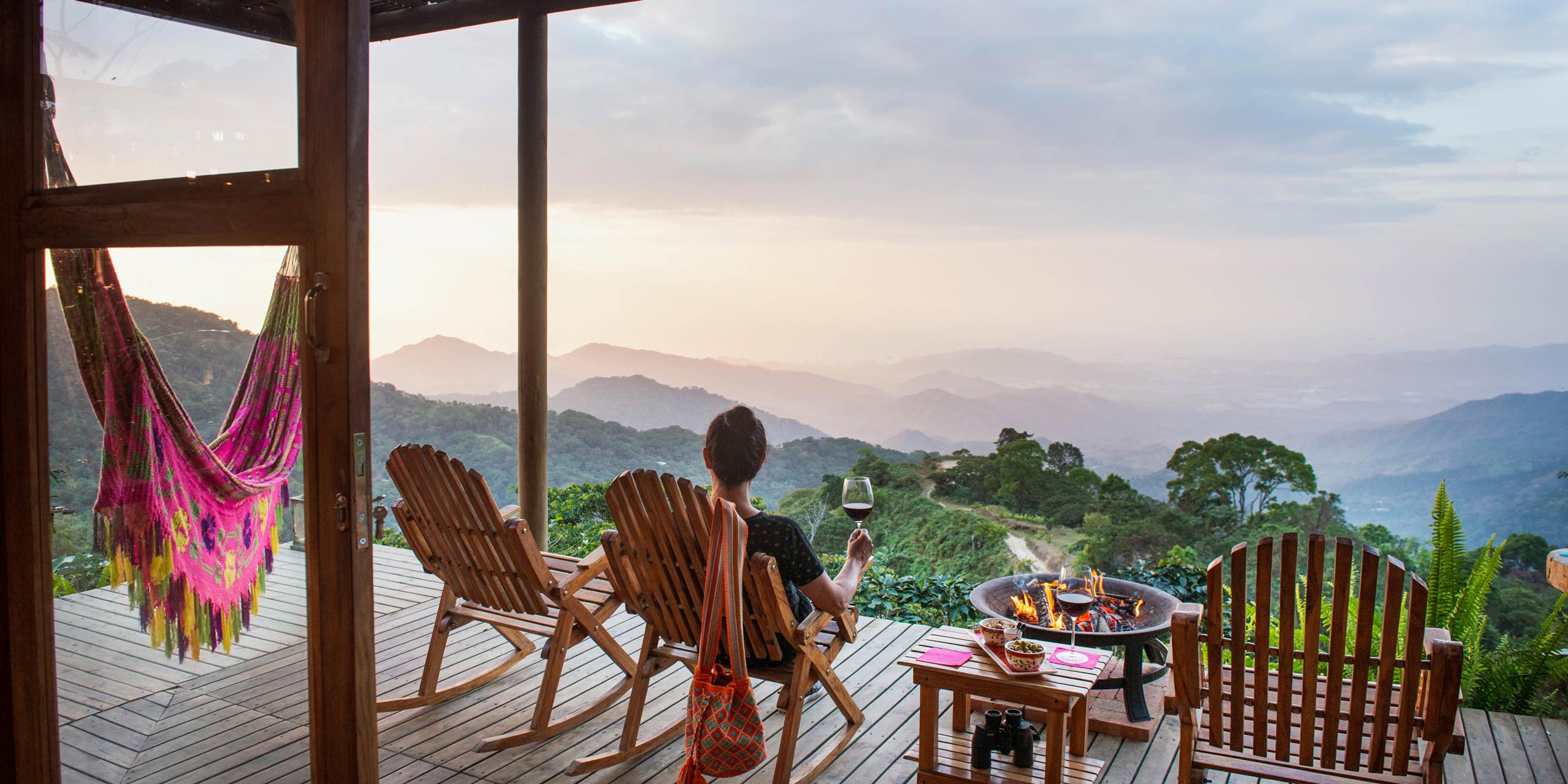 Person on a wooden deck watching the sunset over the Sierra Nevada mountains, wine in hand.