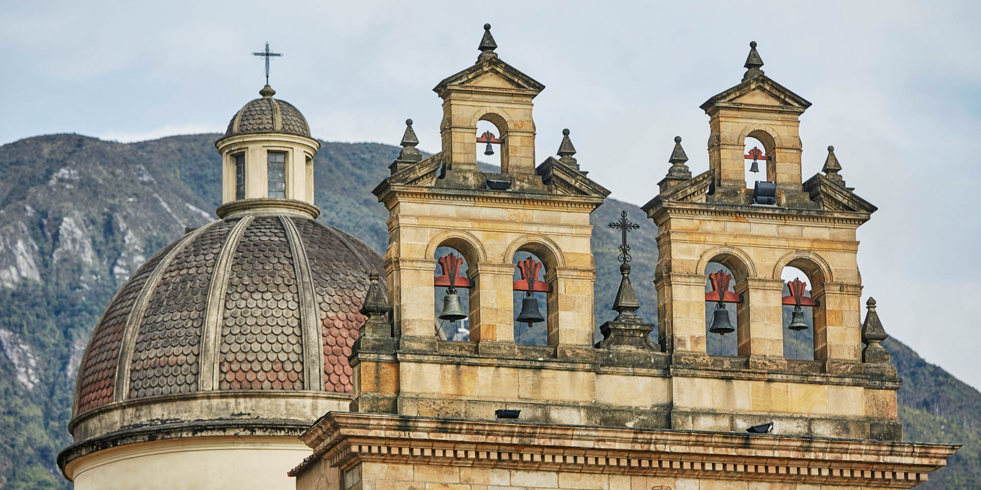 Detail of an ornate stone cathedral's bell towers and dome, set against a backdrop of mountains.