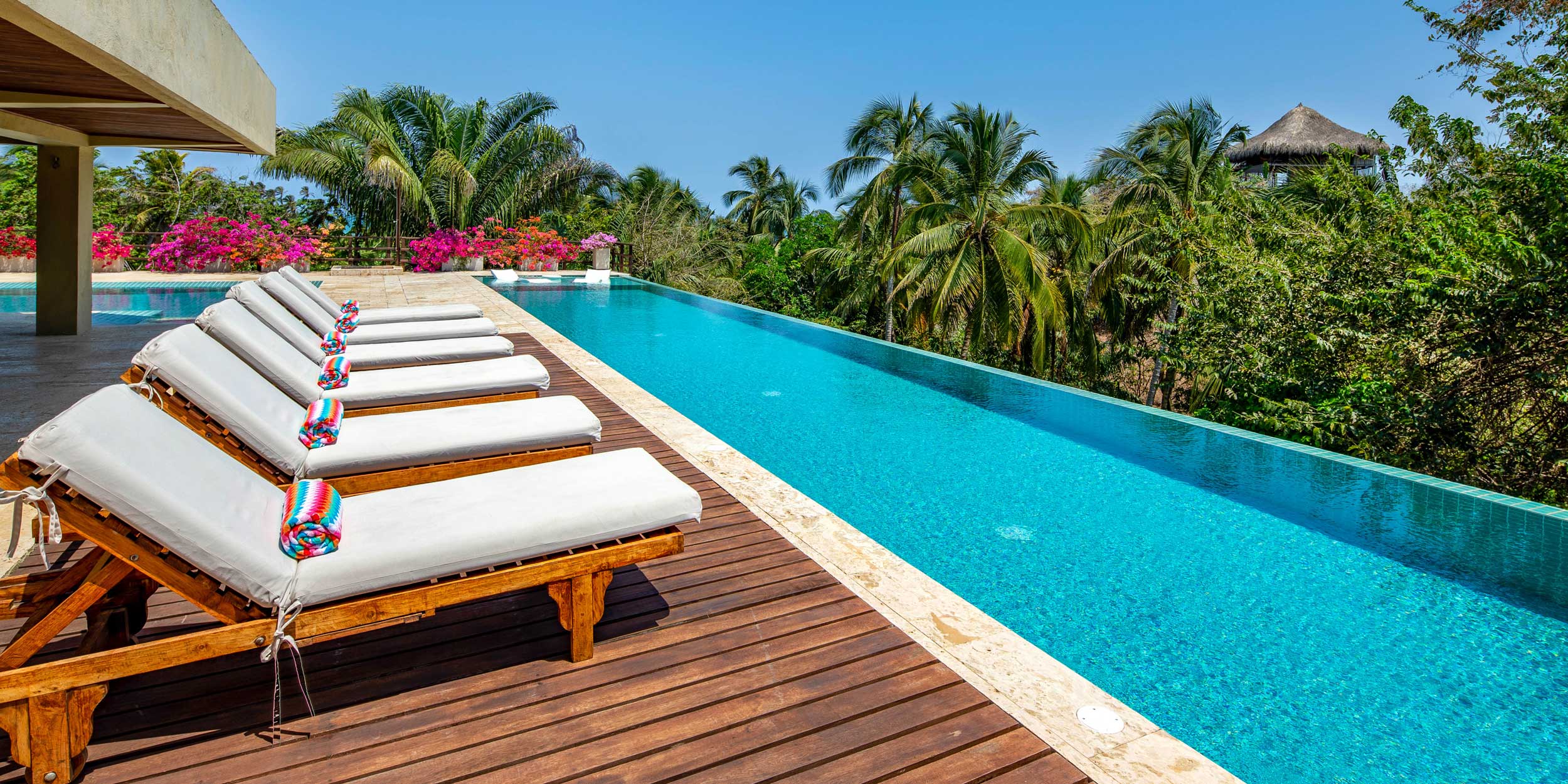 An infinity pool surrounded by lounge chairs and tropical plants at a luxurious villa.