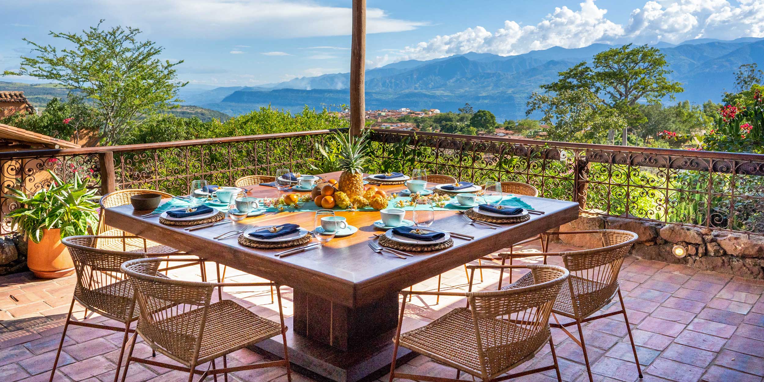 Outdoor dining table set for breakfast on a terrace with a panoramic view of the mountains and a town.