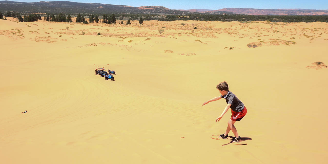 A boy sandboards on a sand dune in Coral Pink Sand Dunes.