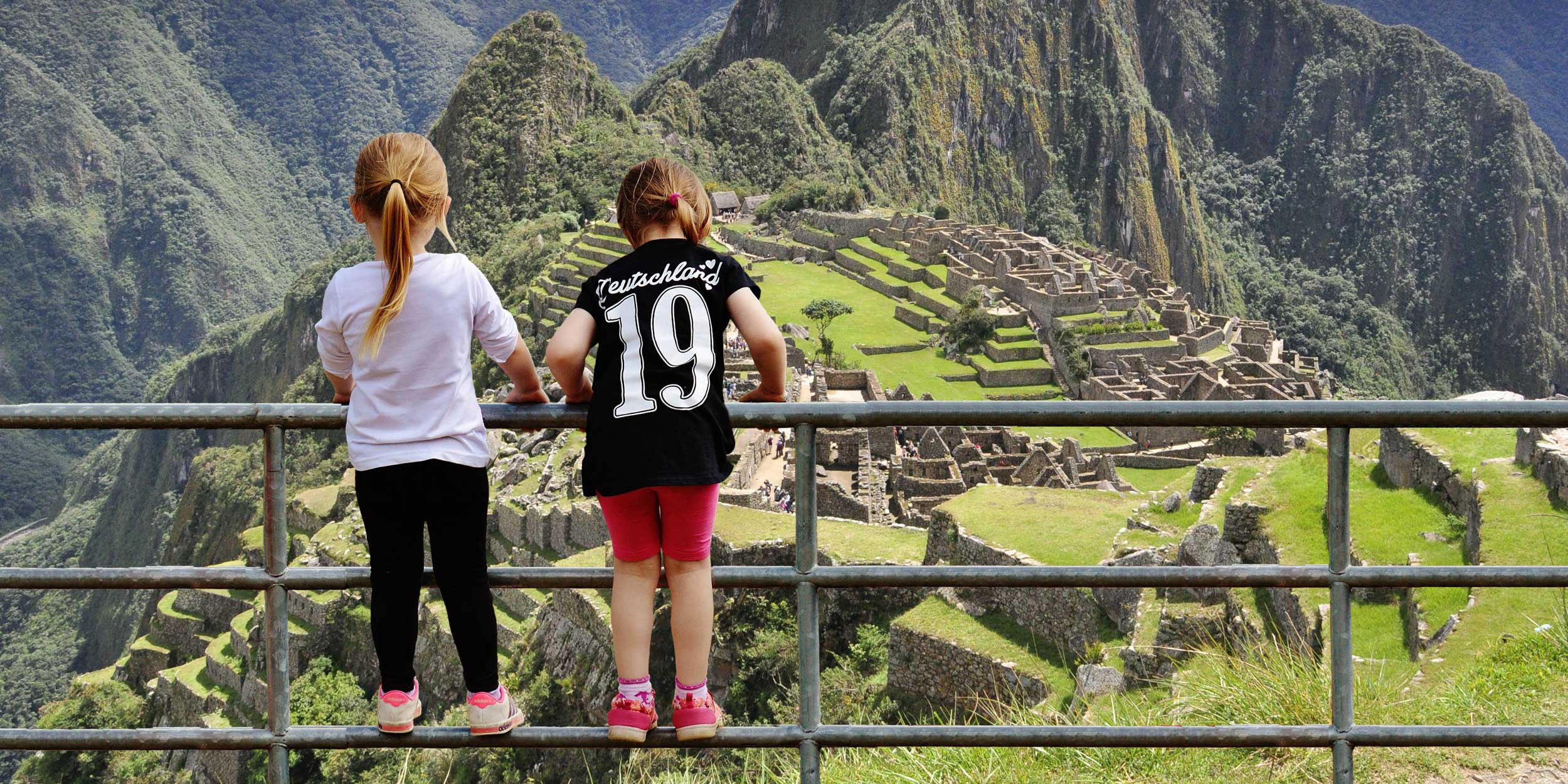 Young girls stand on a railing overlooking Machu Picchu