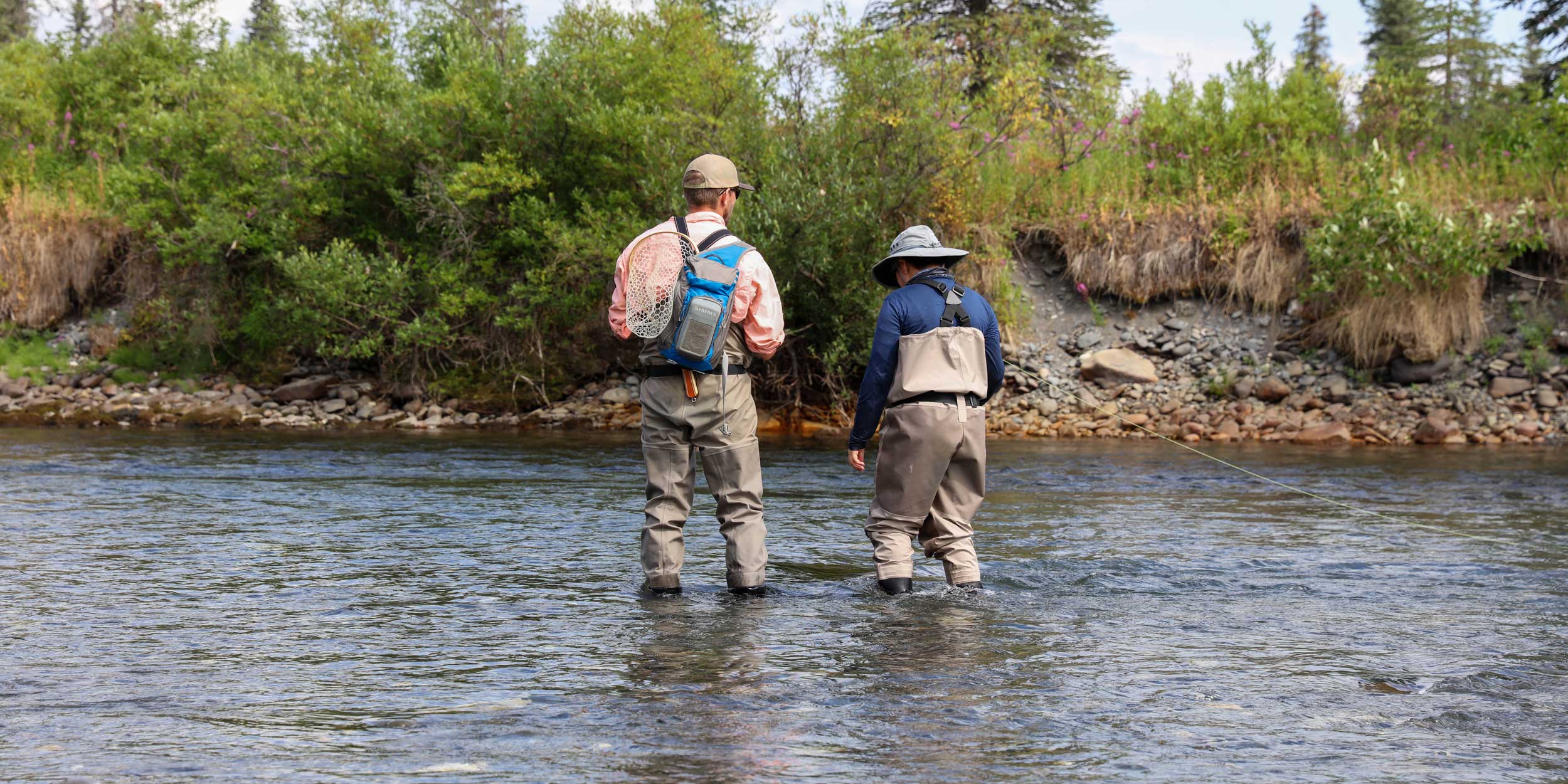 Two men stand in a river to fly fish in Alaska.