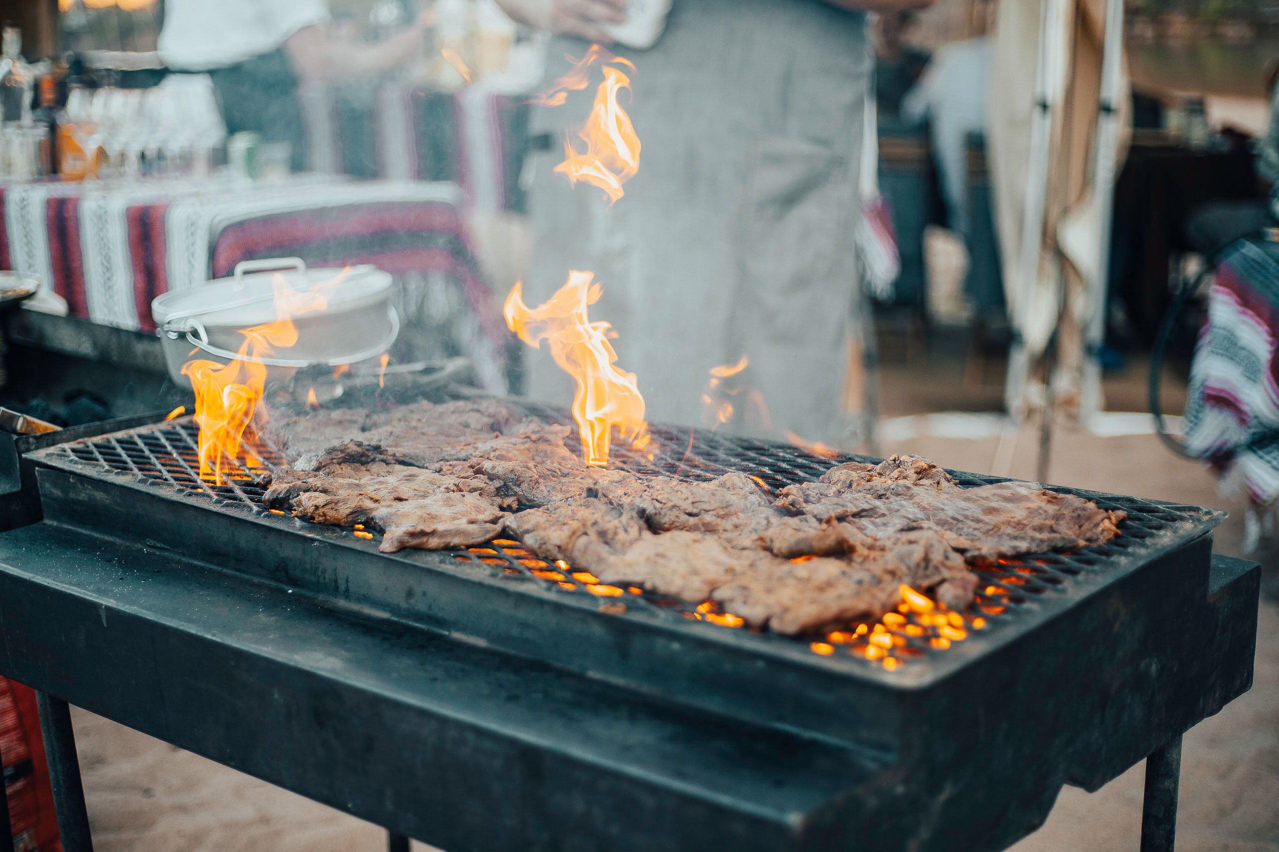Meat roasts over flames on an outdoor grill at a luxury camp.