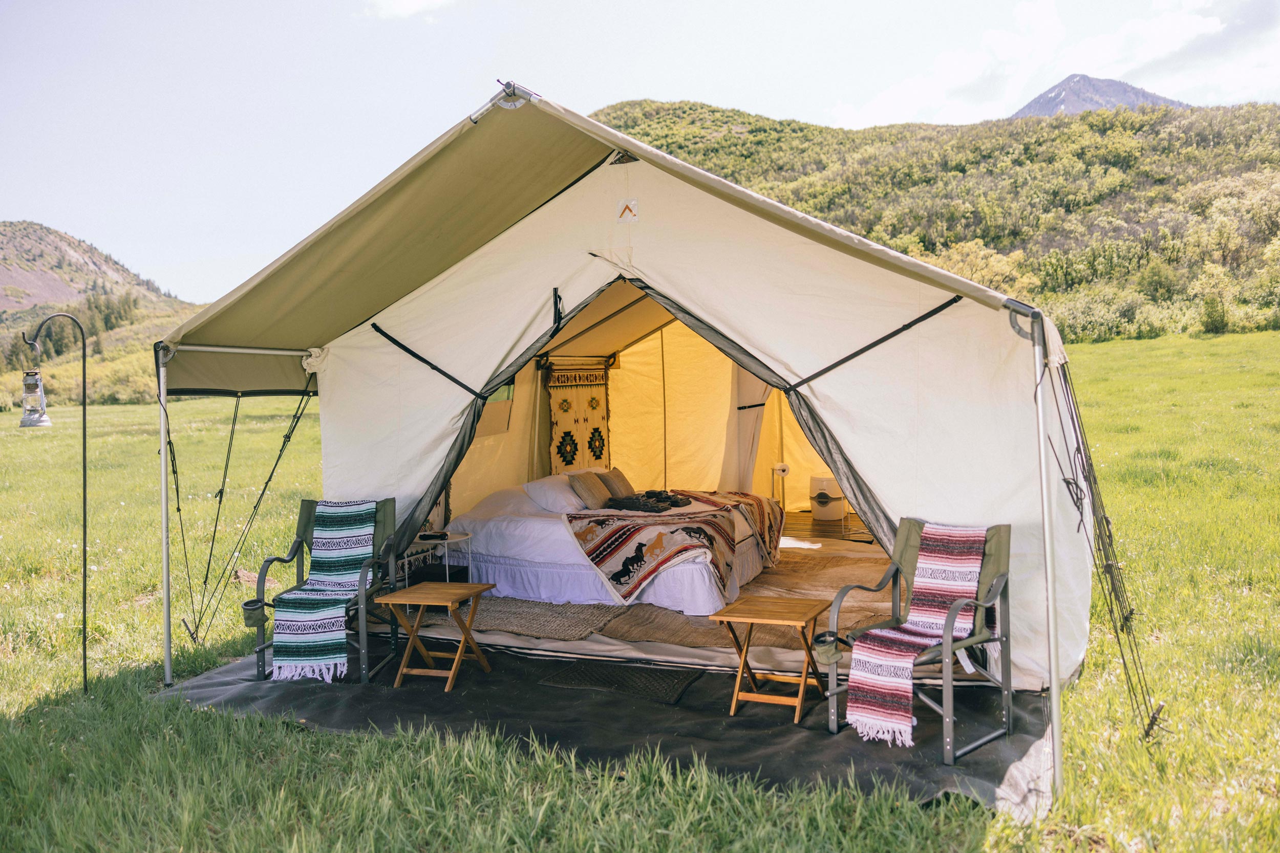 Plush bedding inside of a canvas tent in the middle of field in the Colorado wilderness.