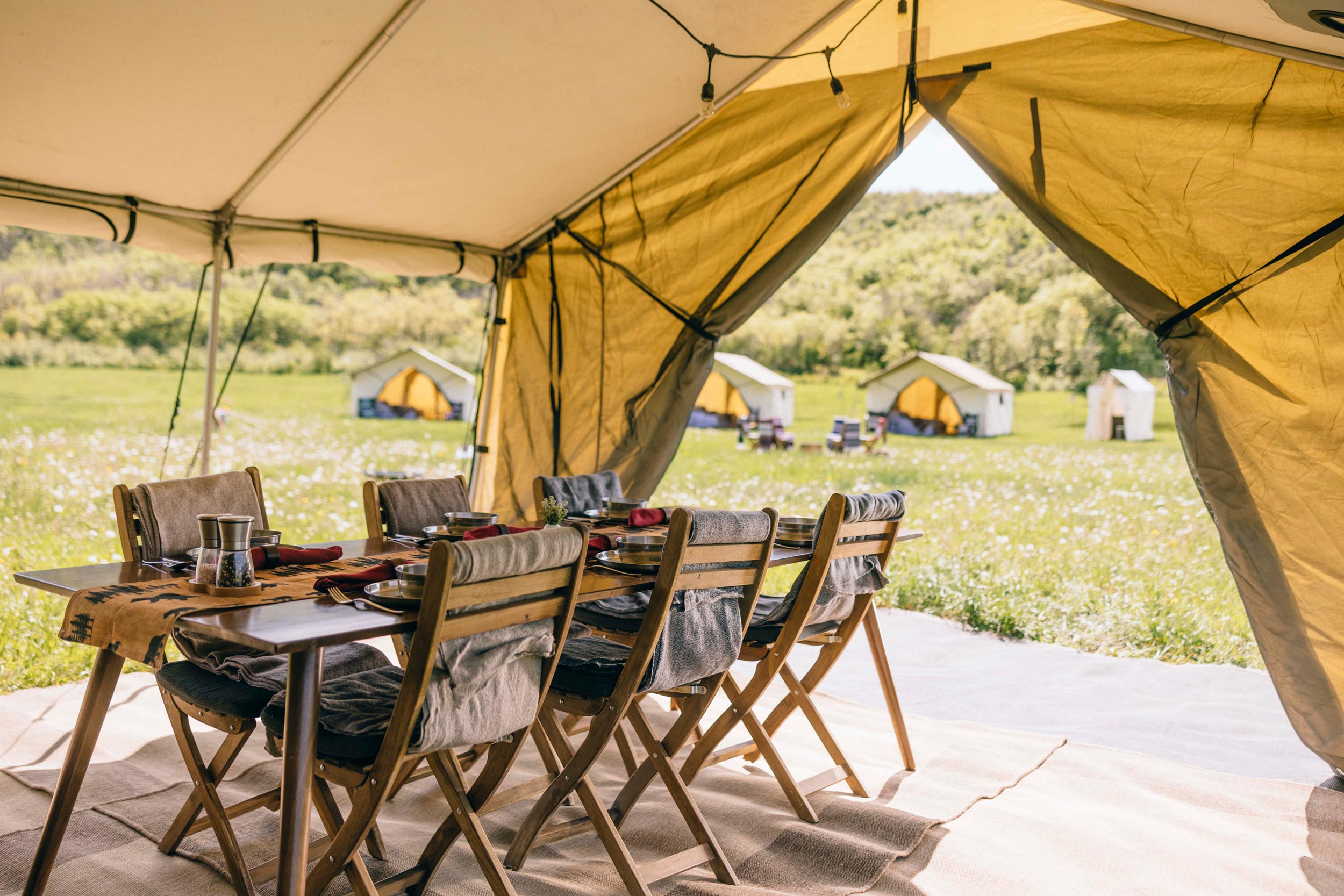 An outdoor dining set-up is seen with a campsite in the background.