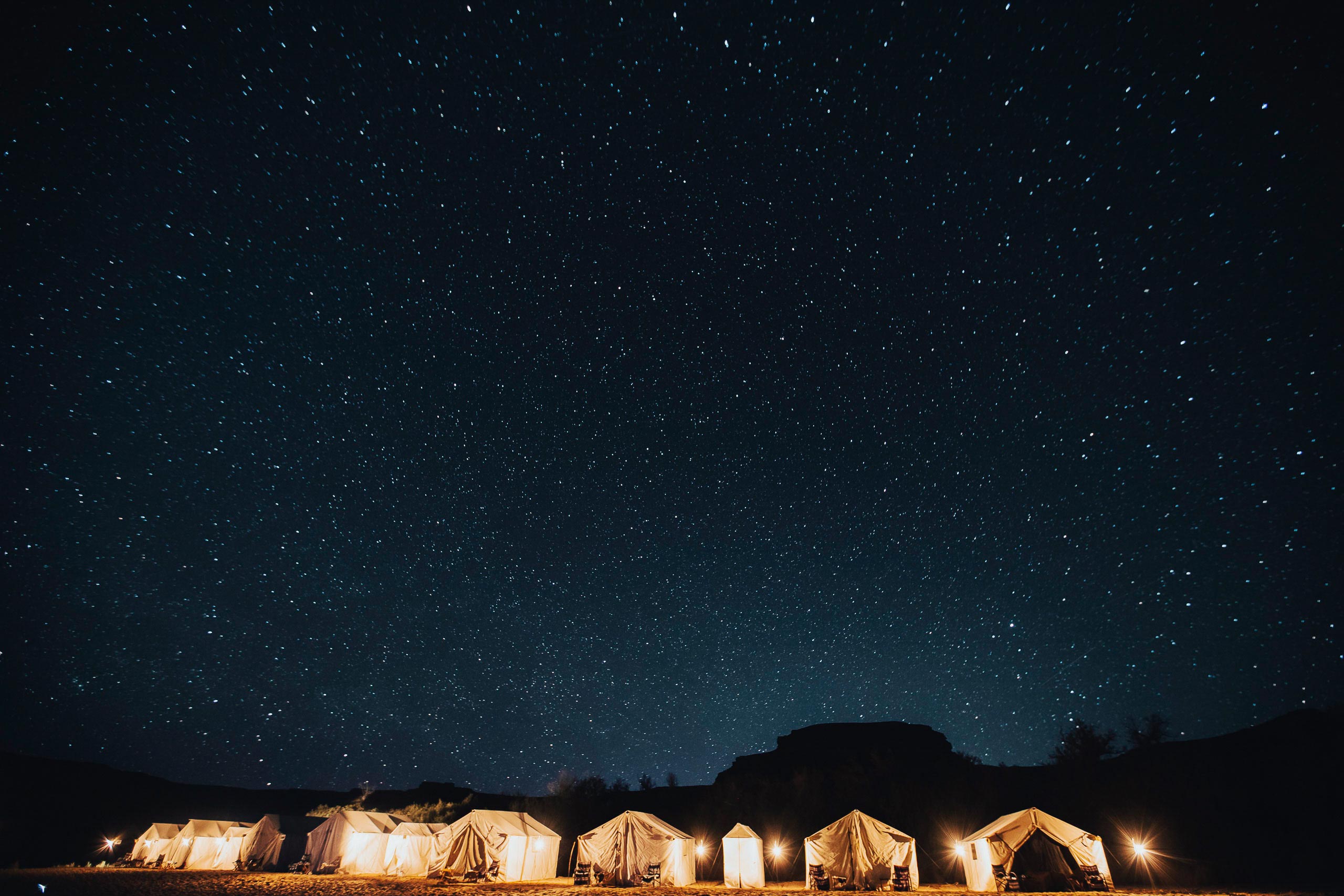Tents are illuminated at night with stars shining brightly above.