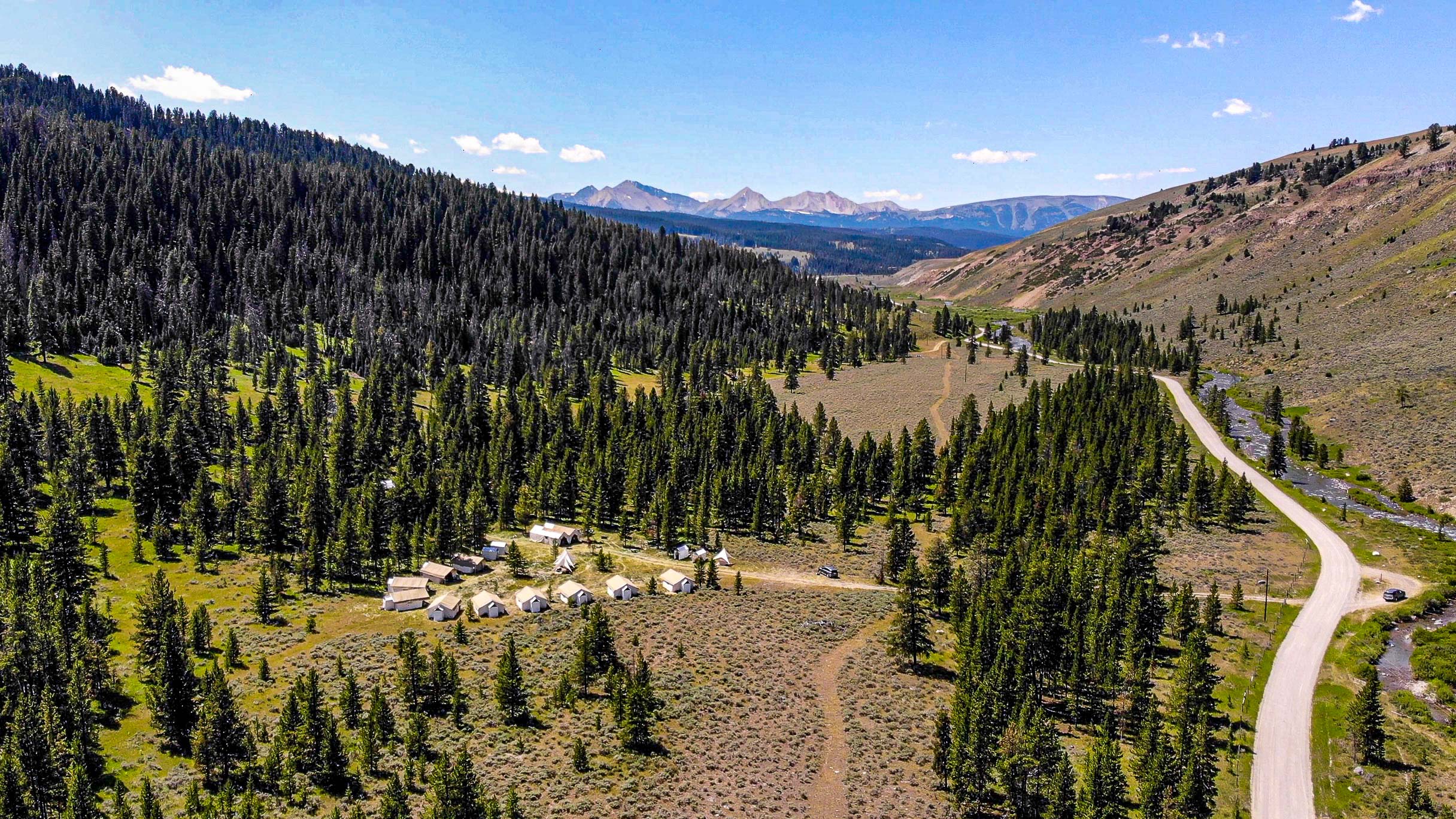 A private tent village is seen from above in a remote area near Yellowstone with forests and mountains surrounding the site.