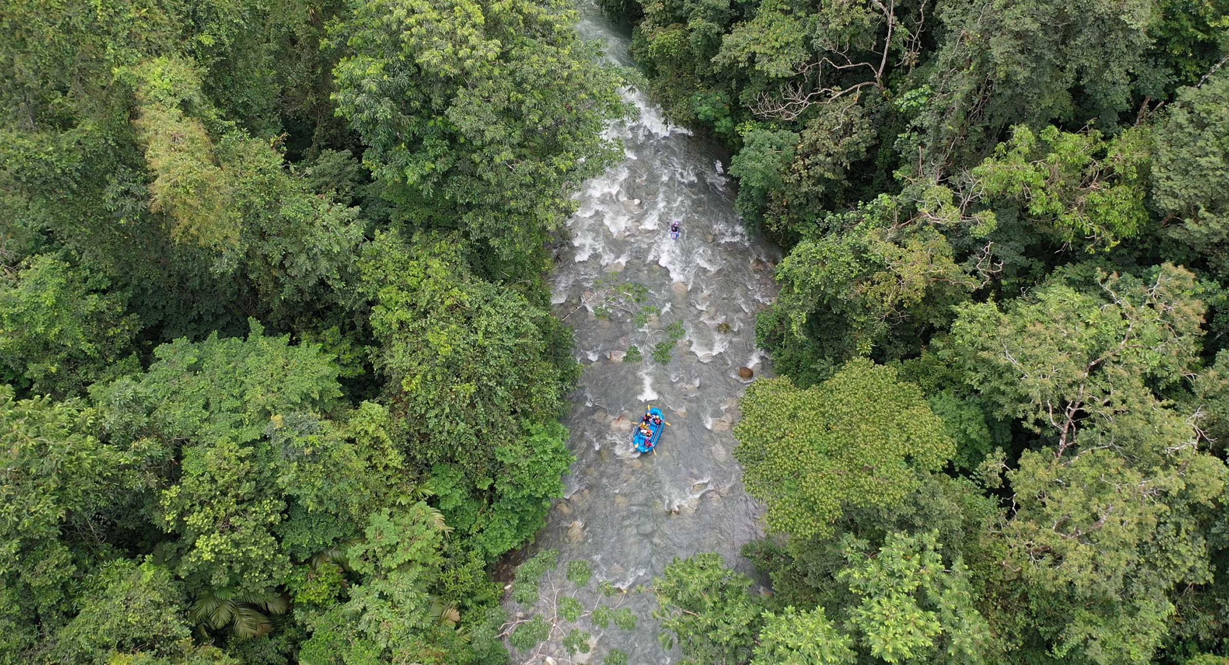 costa-rica-white-water-raftingpng A high-angle view of a blue raft navigating white-water rapids on a jungle river, a staple adventure on a Costa Rica itinerary.