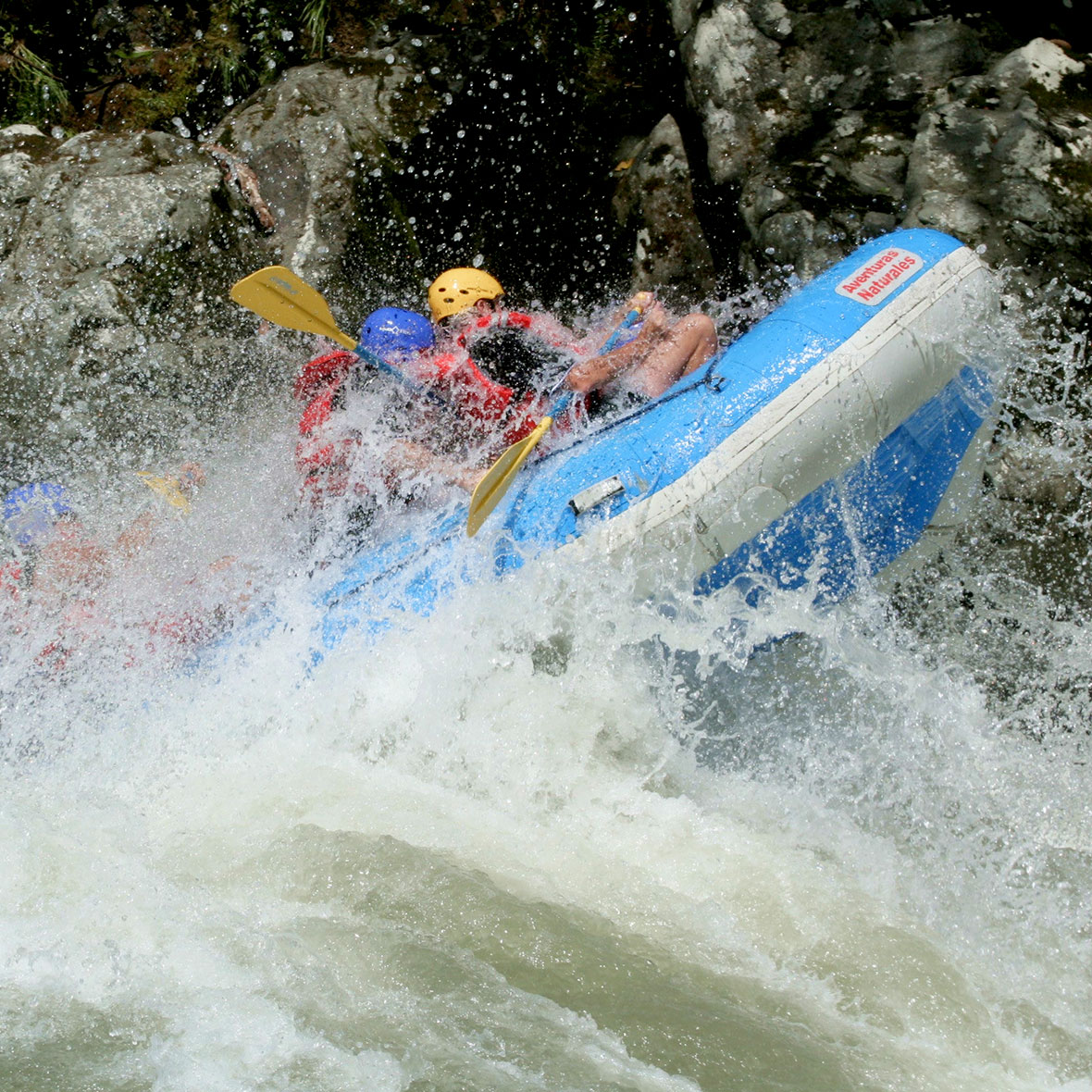 costa-rica-whitewater-rafting-1 Close-up action shot of travelers in a blue raft hitting a massive wave.