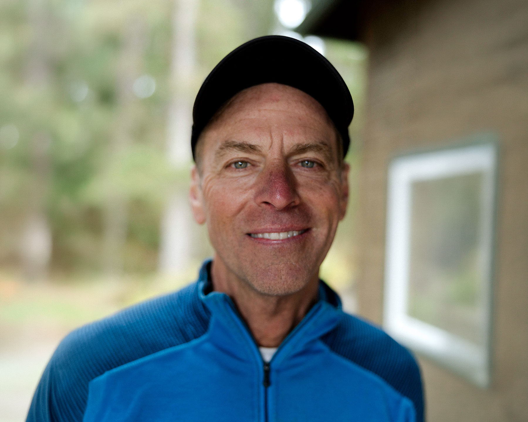 Carter-Atkinson - EXP Journeys Smiling man wearing a black cap and blue zip-up jacket outdoors, facing the camera.