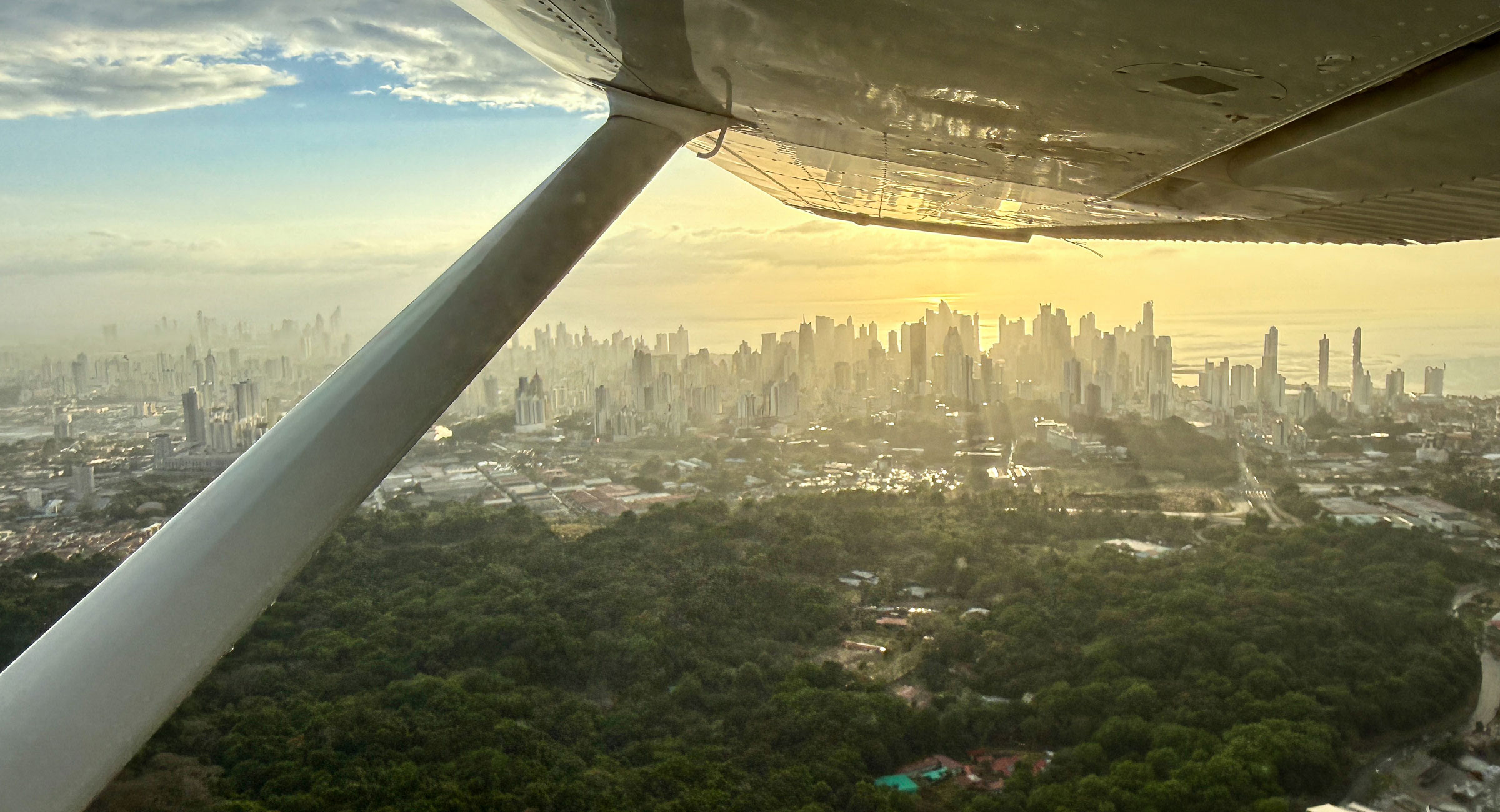 Aerial view of a sunlit city skyline at sunset, seen from the wing of a small airplane.