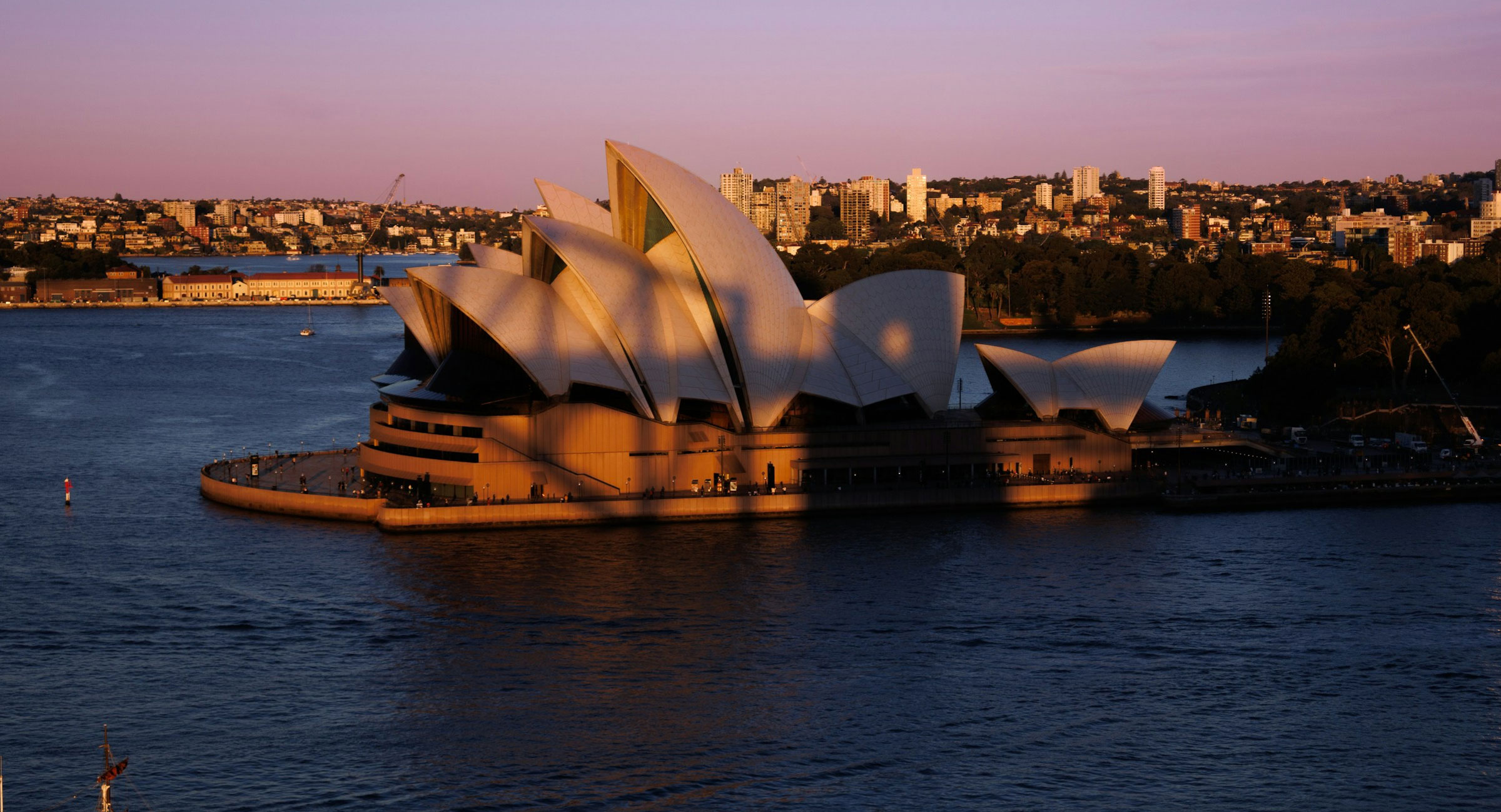 Australia-Sydney-Opera-House - EXP Journeys - EXP Journeys Sydney Opera House at sunset with pink-orange sky over Circular Quay harbor.
